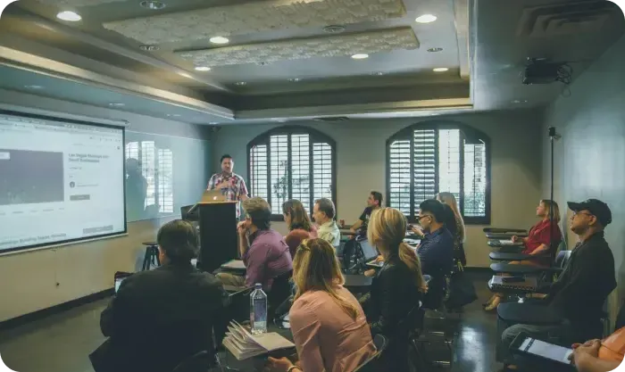 Speaker presenting to a seated audience in a room with a projector screen