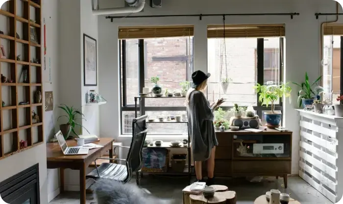 Woman in a hat standing in a bright apartment with a desk and plants