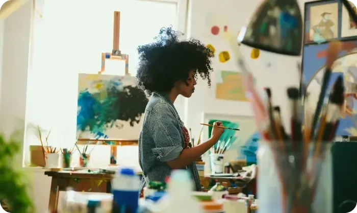 Artist painting at an easel in a studio with brushes in the foreground