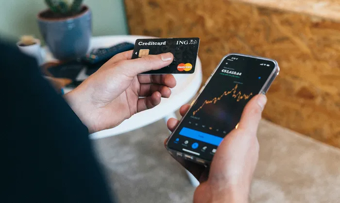 Person holding a credit card in one hand and a phone showing a line chart in the other