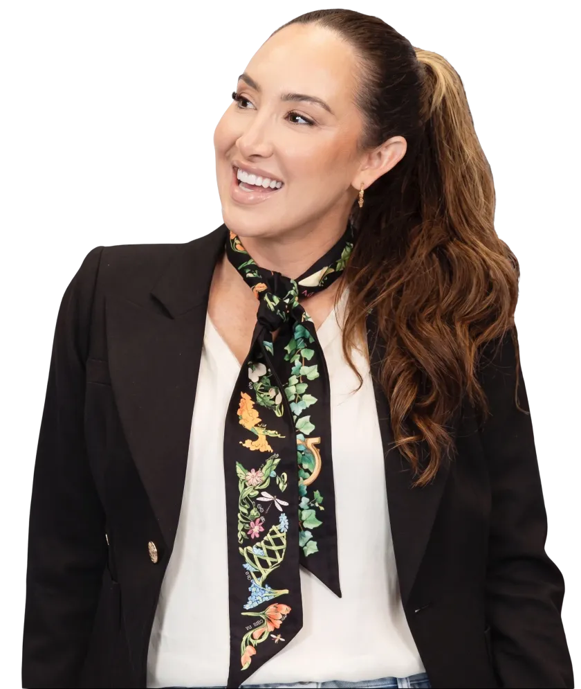 Codie Sanchez in a black blazer and floral scarf, smiling and looking away