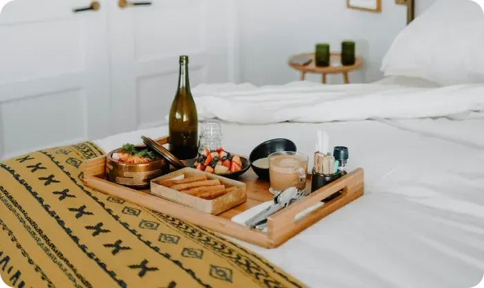 Breakfast tray with fruit, pastries and coffee on a white bed with a yellow patterned throw