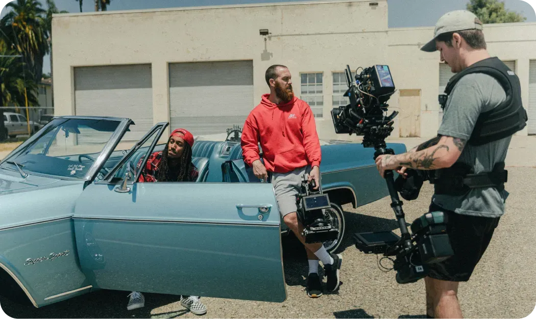 Film crew shooting a man leaning against an open classic blue convertible