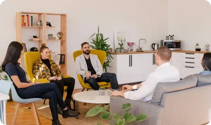 Five people in a bright office lounge having a discussion on yellow chairs and a gray sofa