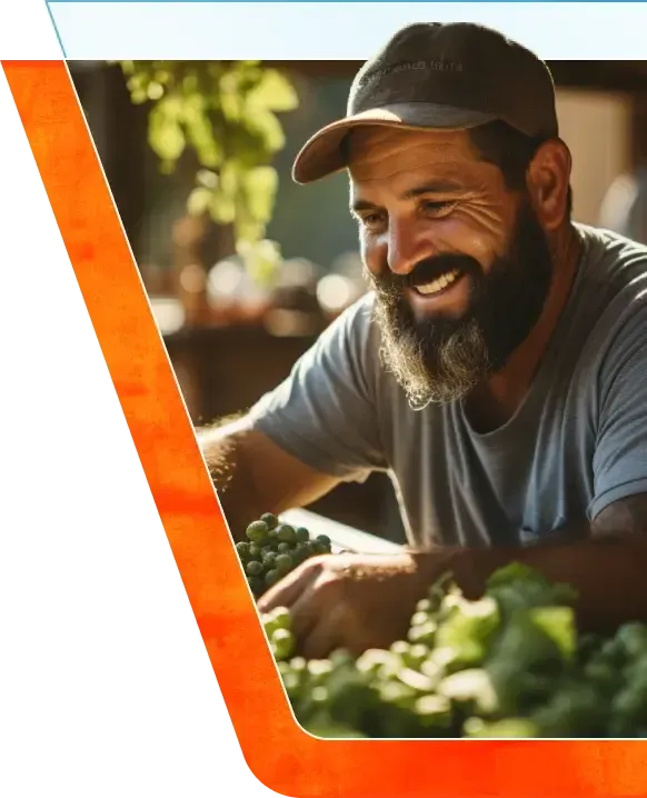Smiling bearded man in a cap handling grapes and greens at a market stall