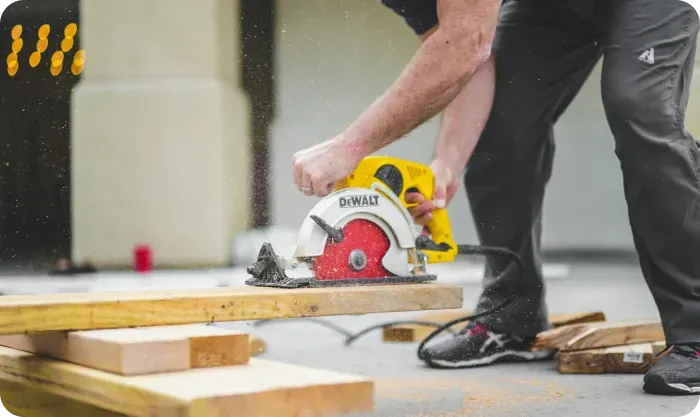 Worker cutting a wood plank with a yellow circular saw, sawdust in the air