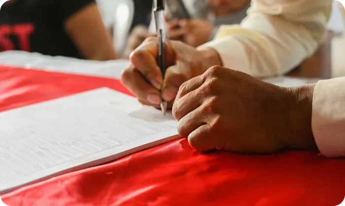 Hands signing papers on a table covered with a red cloth