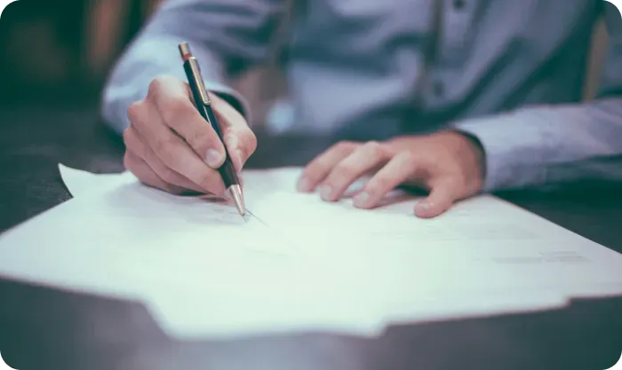 Person signing a document with a pen at a dark table