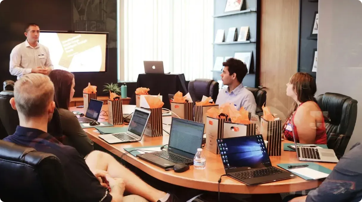 Man Standing In Front Of People Sitting Beside Table With Laptop Computers Gmsnxqiljp4