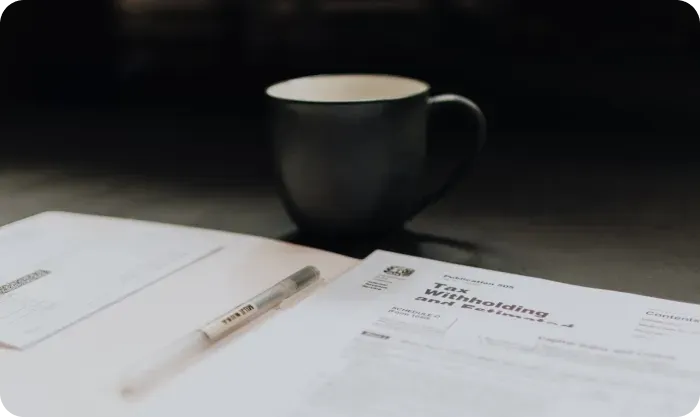 Tax withholding form and a pen on a desk beside a dark coffee mug