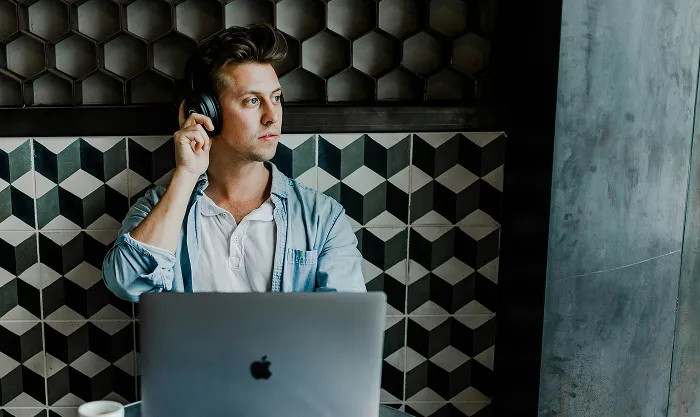 Man with headphones pausing from his laptop and looking away thoughtfully