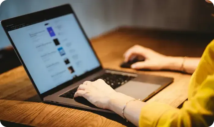 Person Browsing Website On Laptop At Wooden Desk