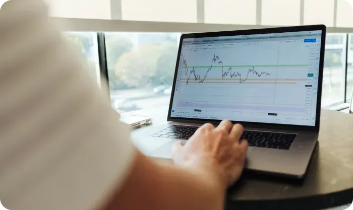 Person using a laptop displaying a stock price chart beside a window