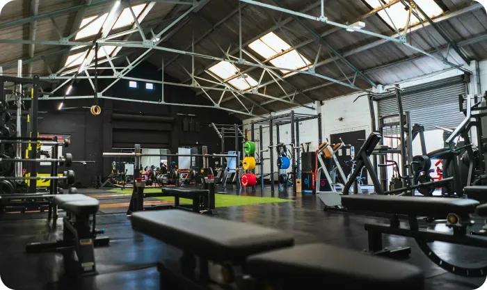 Spacious gym with weight benches, racks and colorful weight plates under a skylit roof