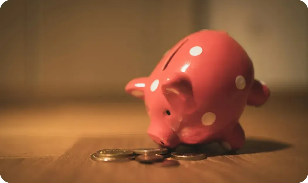 Pink polka-dot piggy bank with a few coins on a wooden table