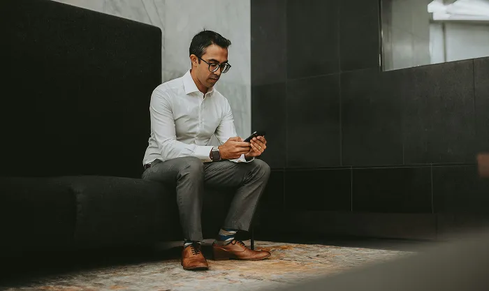 Man in a white shirt sitting on a dark bench looking at his phone