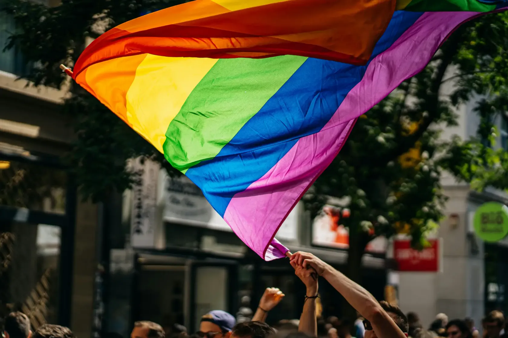 Rainbow pride flag waving above a crowd on a city street