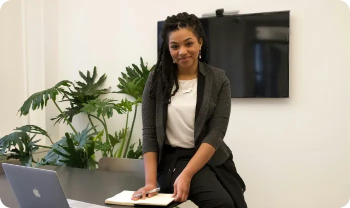 Smiling woman in a blazer sitting on a table with a notebook and pen