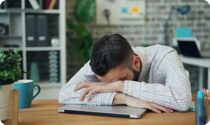 Man resting his head on his arms over a closed laptop at his desk