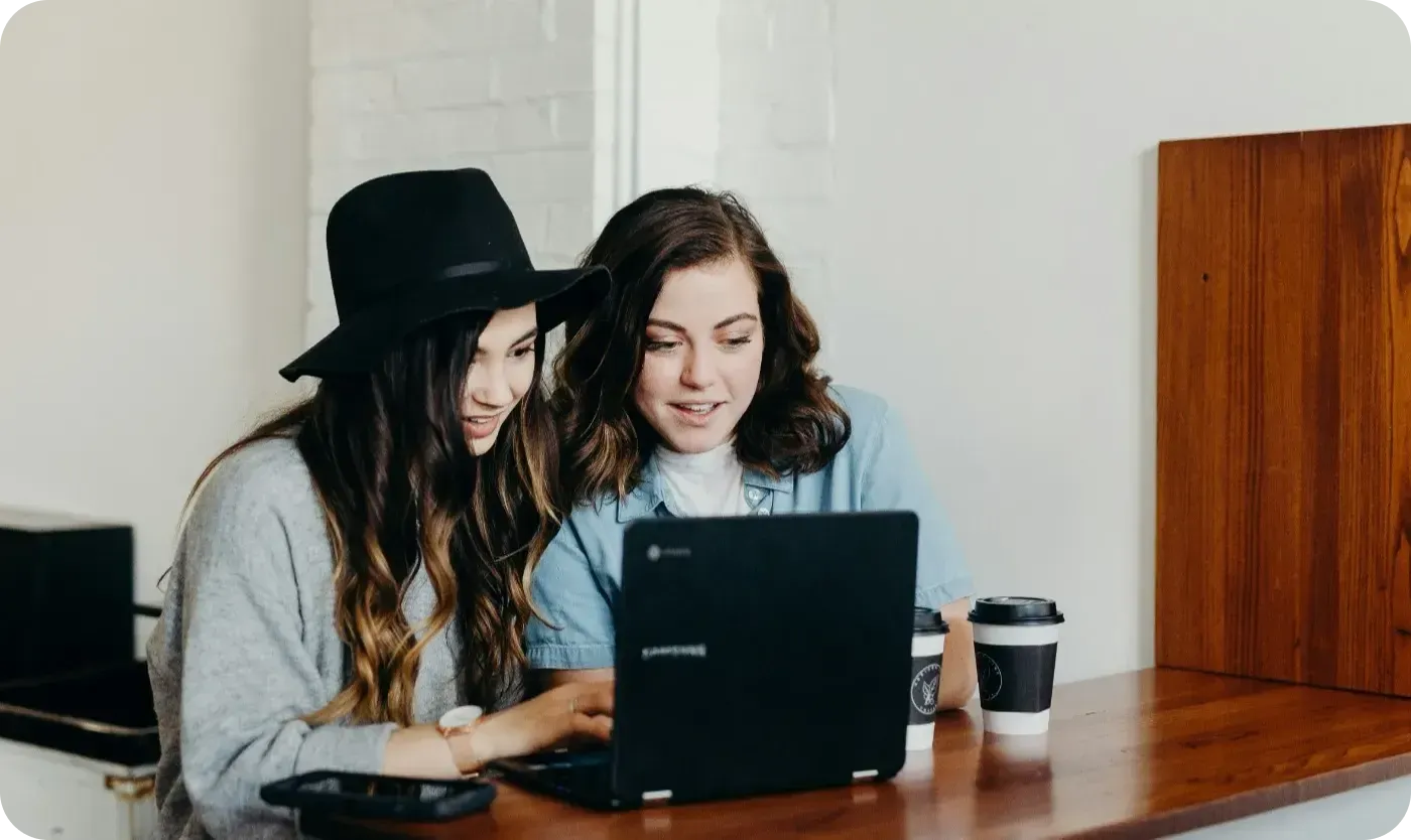 Two women looking at a laptop together at a café counter with takeaway coffees