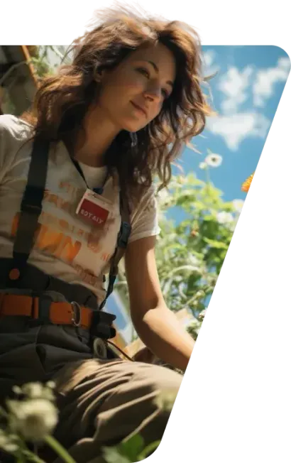Smiling woman in suspenders and a t-shirt crouching among flowers under a blue sky