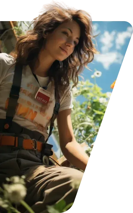 Smiling woman in suspenders and a t-shirt crouching among flowers under a blue sky