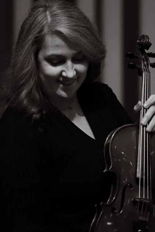 Black-and-white portrait of a smiling woman looking down while holding a violin