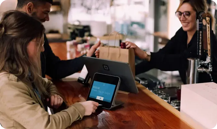 Customer paying at a counter by card terminal while a smiling worker hands over a paper bag