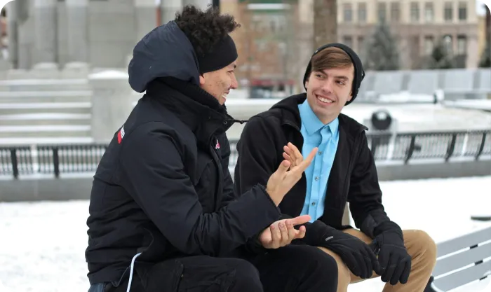 Two friends having a conversation on a bench in a winter setting.