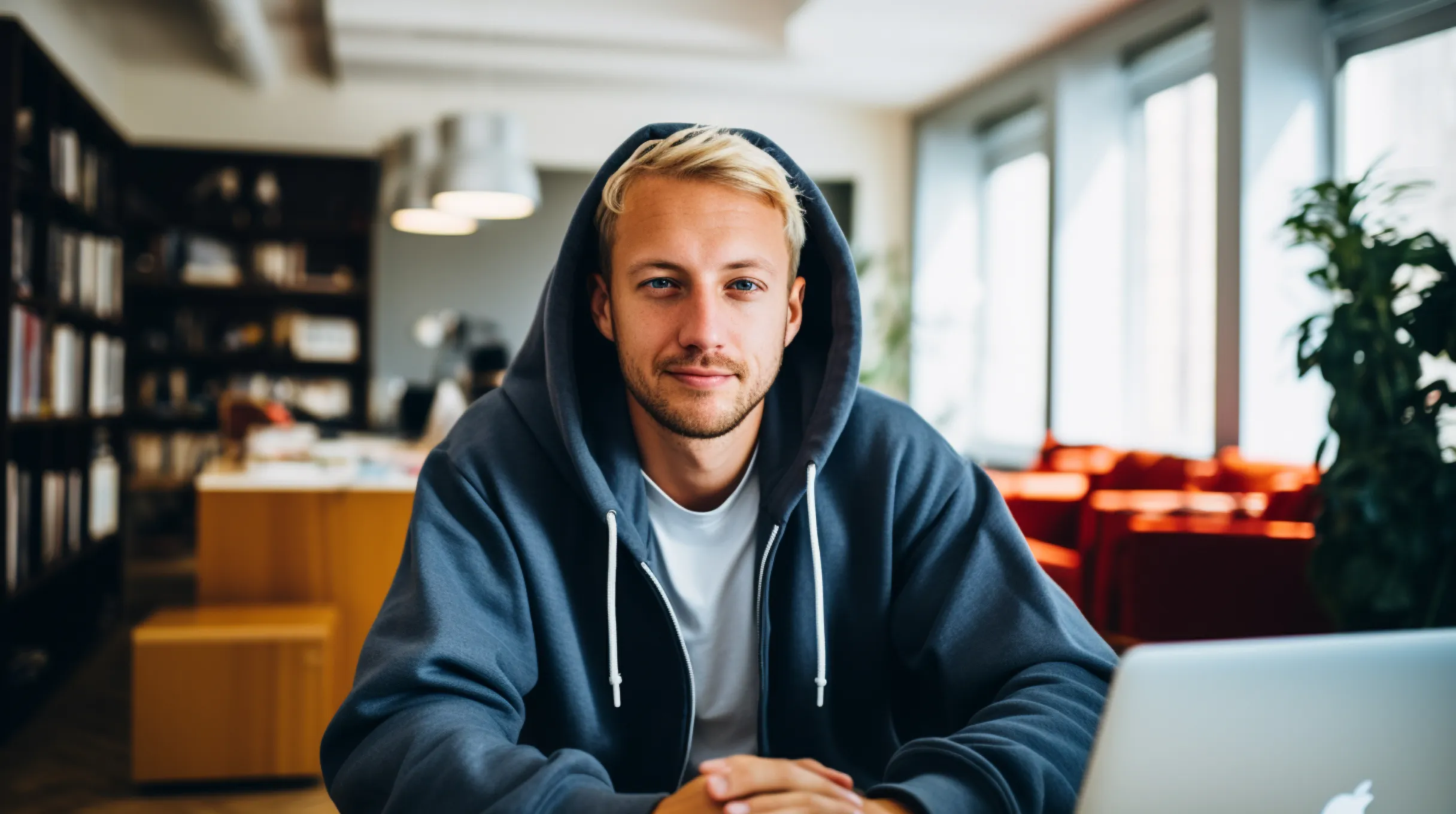 A person wearing a hoodie sits at a table, focused on a laptop.