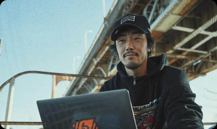 A man sitting using a laptop, with the bridge in the background.