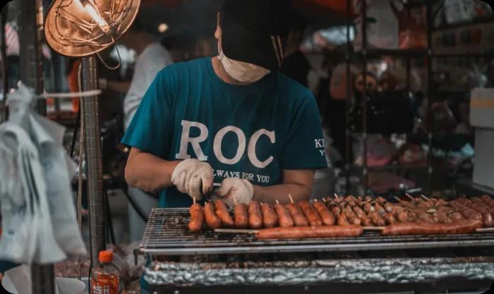 A man tending to a grill, grilling sausages profesionally