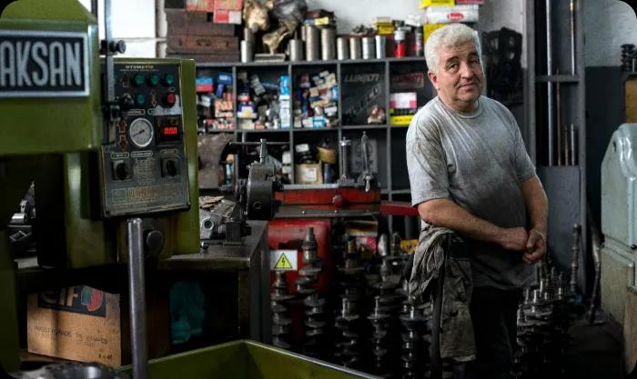 A man stands in a workshop, focused on operating a machine surrounded by tools and equipment.