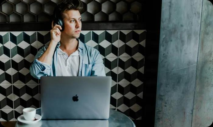  A man seated at a table, working on a laptop, with a coffee cup beside him, focused on his task.