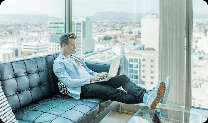 A man seated on a couch, focused on his laptop, creating a relaxed yet productive atmosphere in his living space.