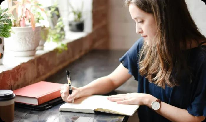 A woman focused on writing in a notebook, capturing her thoughts with a pen in a serene environment.