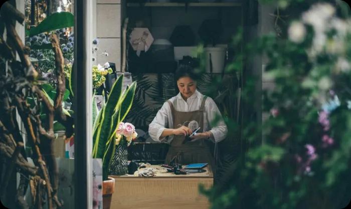 An asian woman working at a desk in what appears to be a flower shop