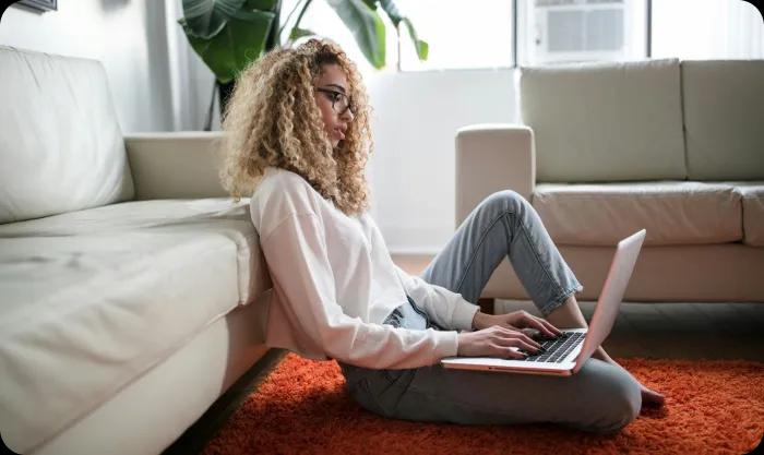 A woman seated on the floor, focused on her laptop, surrounded by a cozy and inviting atmosphere.