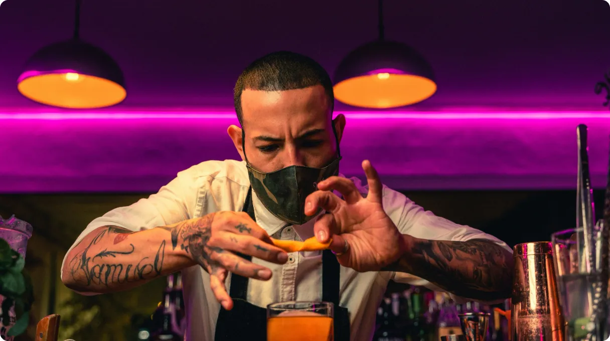 A masked bartender holding an orange, ready to serve.