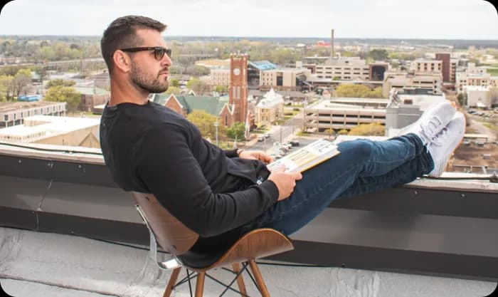 Man with sunglasses and book sitting on balcony