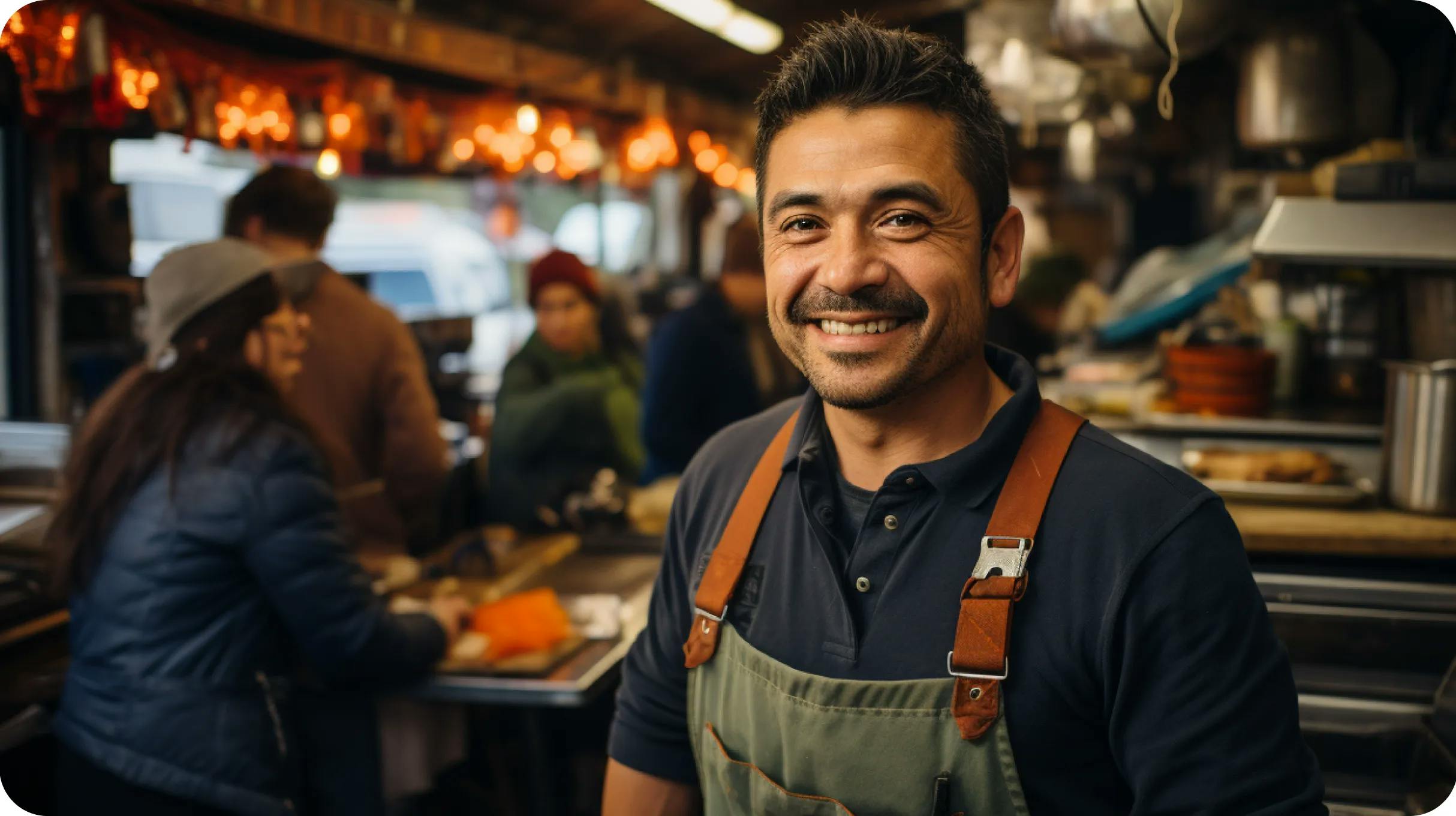 A man smiling to the camera, working at the coffee shop with lots of customers in the background