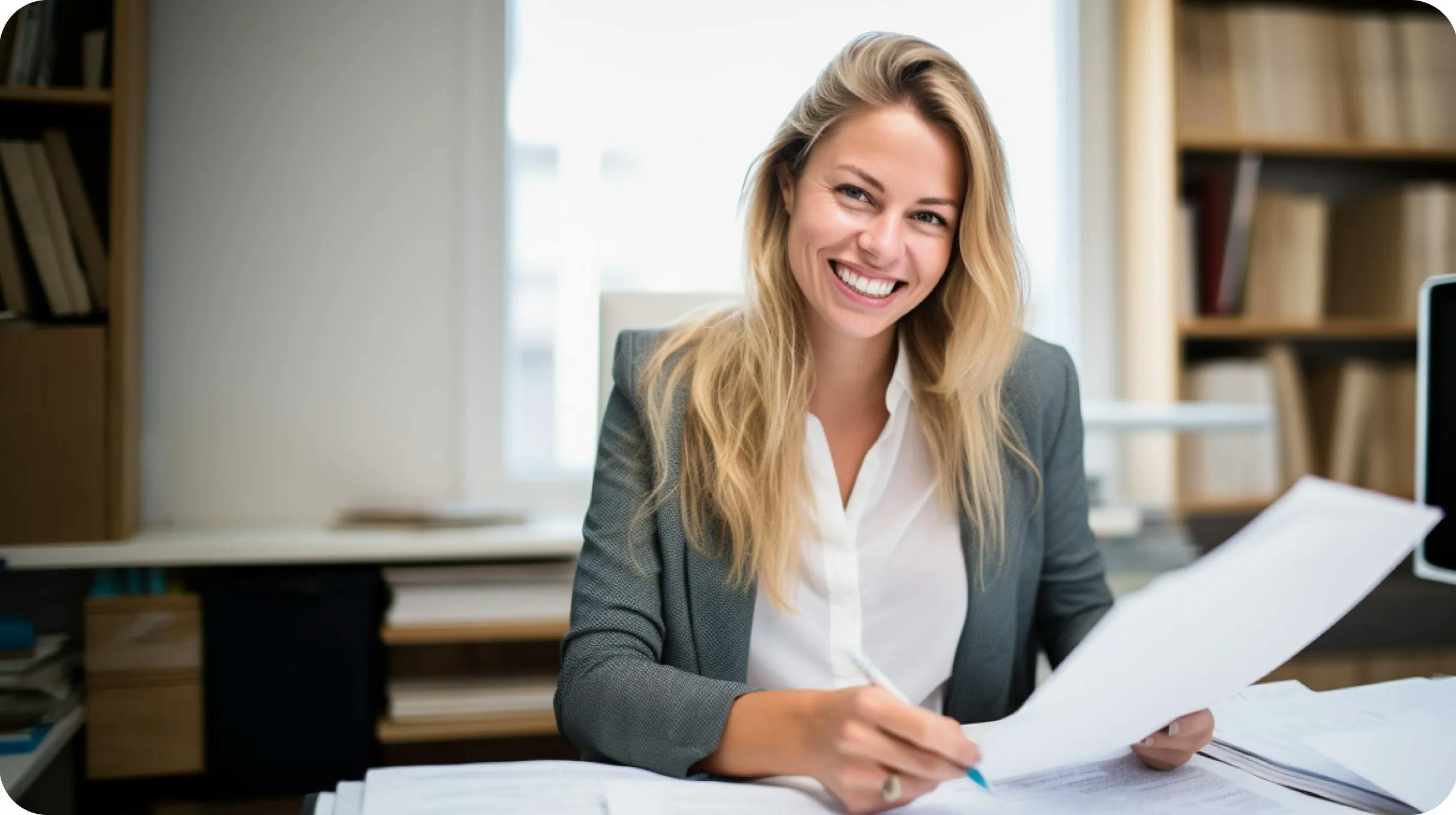 Smiling woman looking at the camera, holding some company paperwork in an office