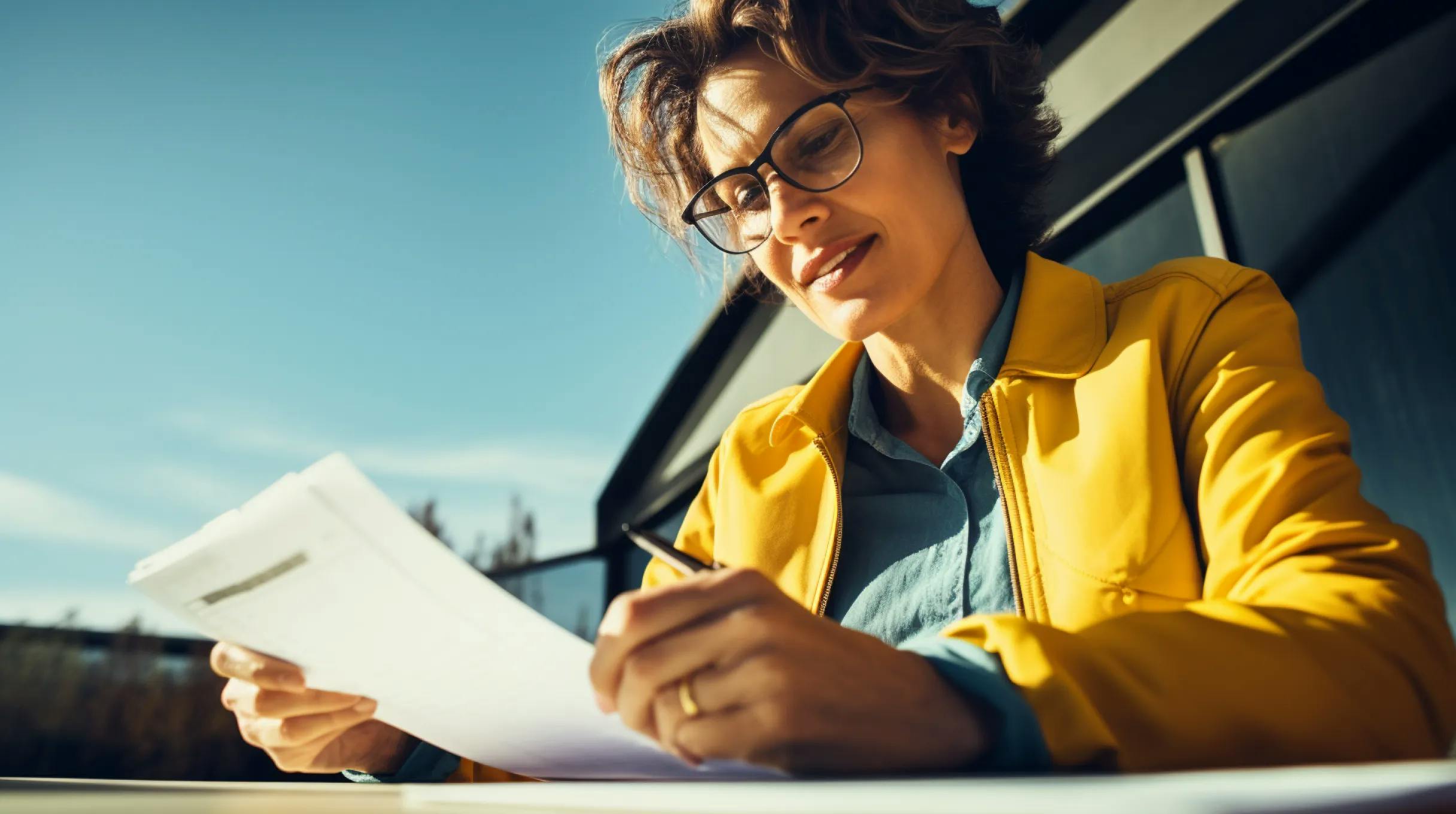 A woman wearing glasses is focused on reading a document, displaying attentiveness and concentration.