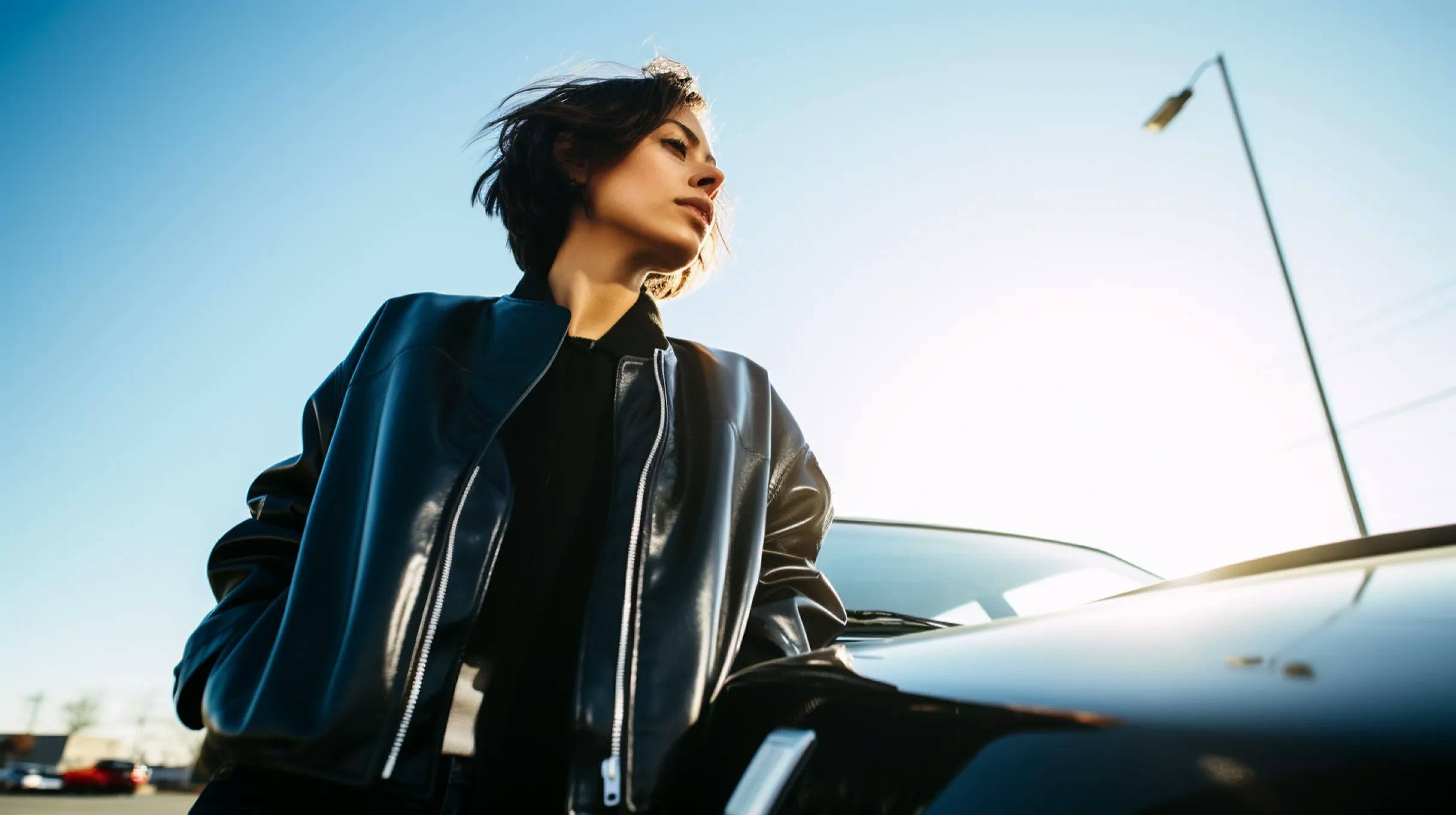 A woman in a leather jacket standing next to a car.