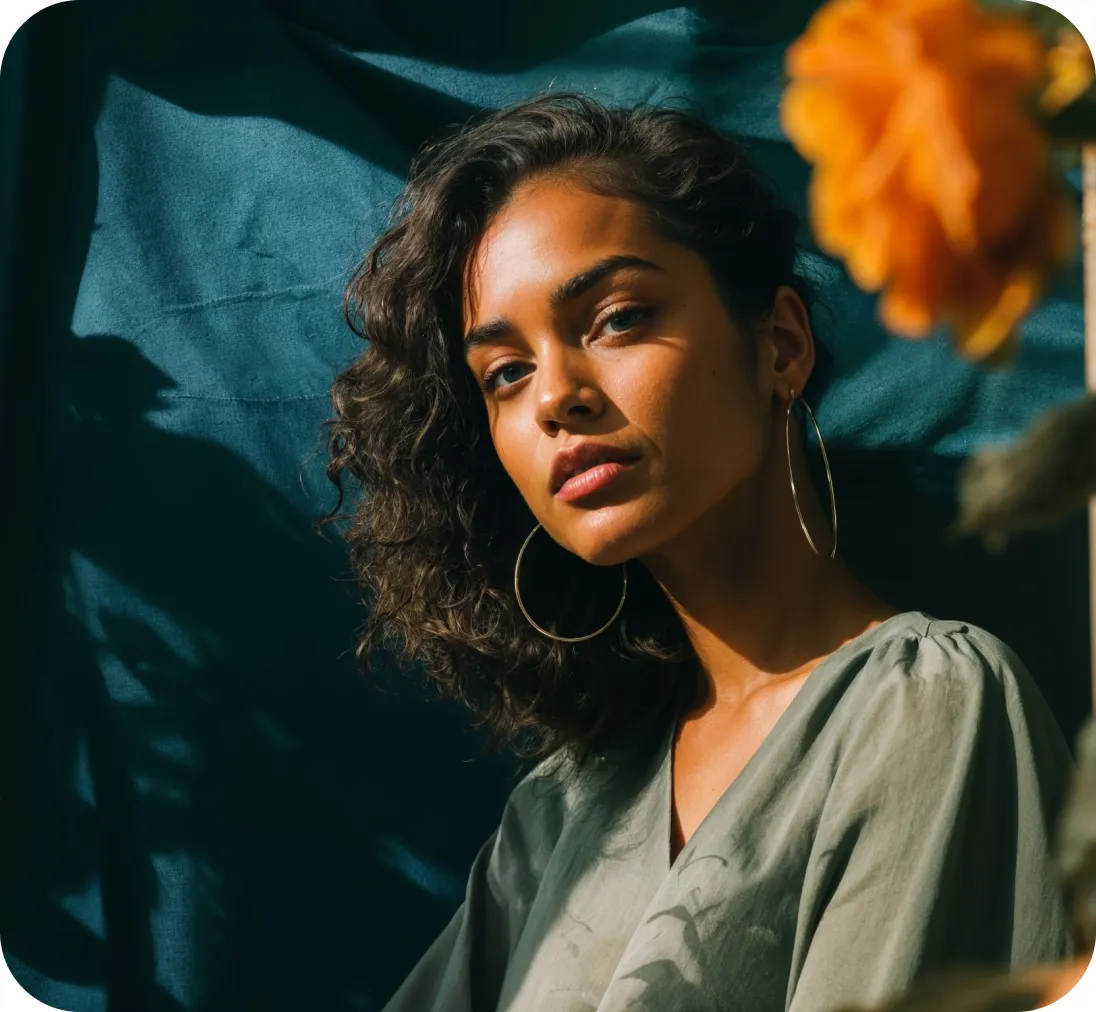 Woman with curly hair and hoop earrings, posed against a teal backdrop.