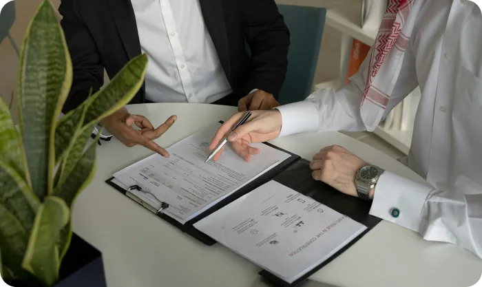 Two men sitting at table with papers and a pen