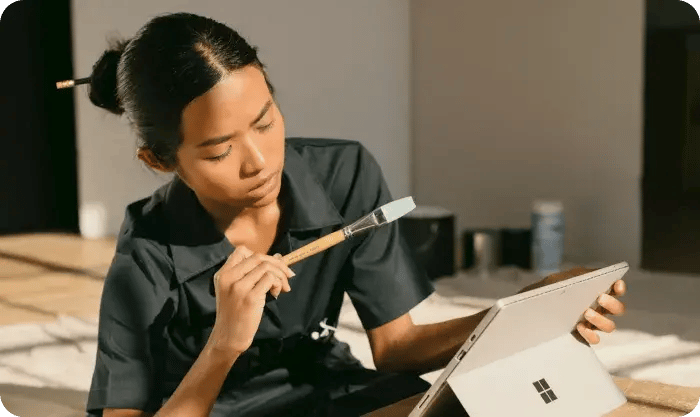 A Woman Sitting On A Box Holding A Paintbrush