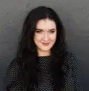 Carrie Buchholz-Powers smiling in front of a dark gray background