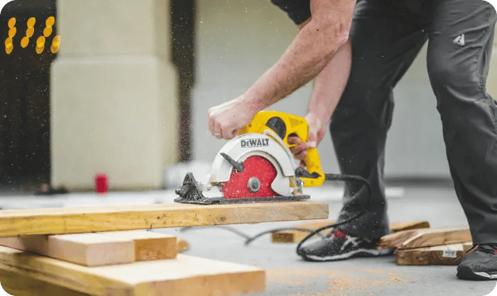 Man In Black Sweatpants Using Dewalt Circular Saw And Cutting A Wood Plank