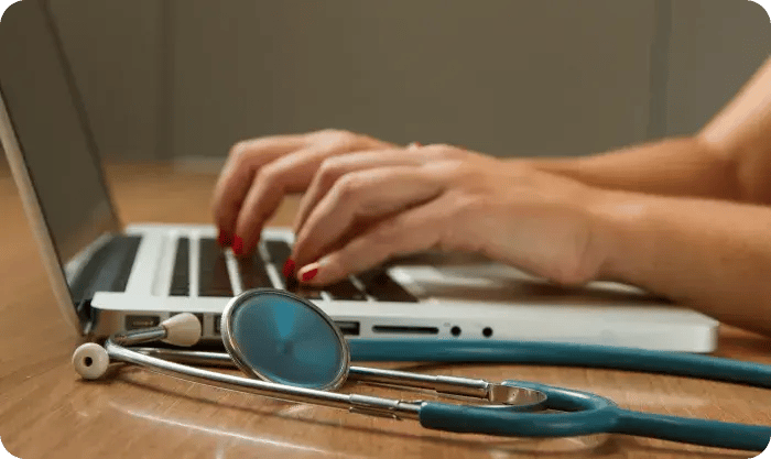 Hands Typing On Laptop With Stethoscope On Desk